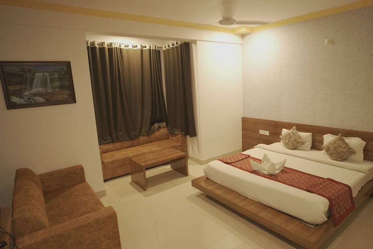 A hotel room with a bed, a sofa, a small table, and a painting on the wall.