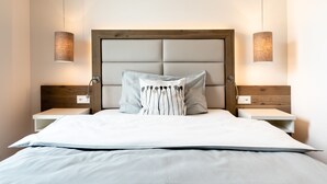 Une chambre à coucher moderne avec un grand lit, une tête de lit en bois, deux tables de chevet et deux lampes fixées au mur.