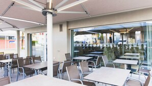 Un café en plein air avec des tables et des chaises, de grandes fenêtres et un ventilateur de plafond.
