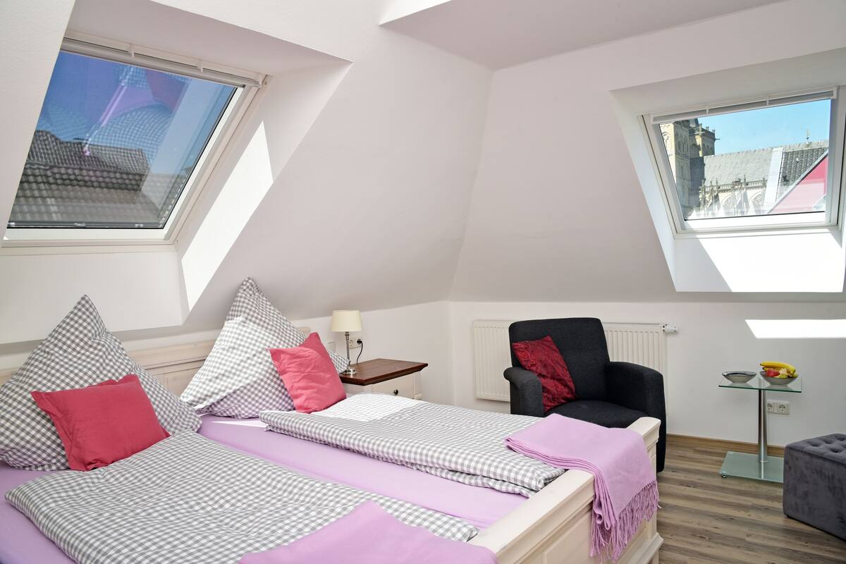 A bedroom with a bed, a chair, a small table, and a window.