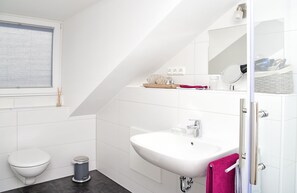 Un baño moderno con lavamanos, inodoro y zona de ducha blancos.