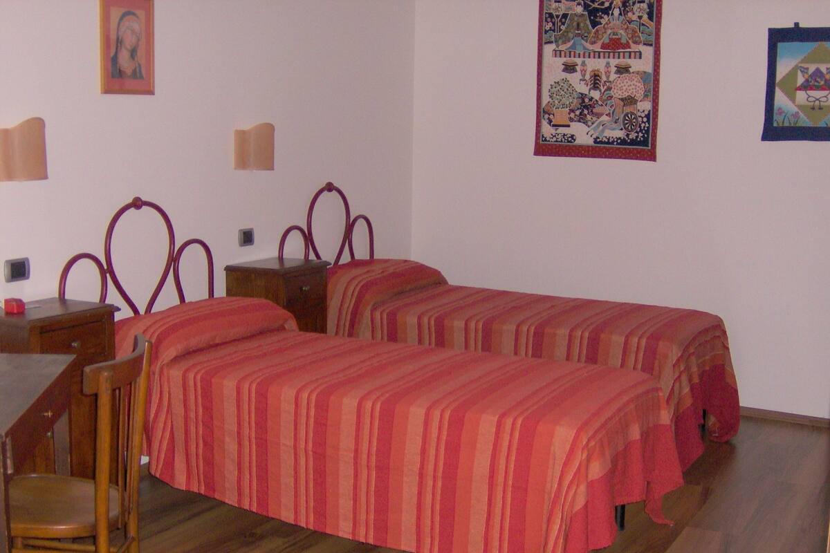 A bedroom with two single beds, a wooden desk, a chair, and a small bedside table.