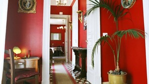 A hallway with red walls, a wooden desk with a lamp, a chair, and a potted plant. - 5 Balconi (Catania)