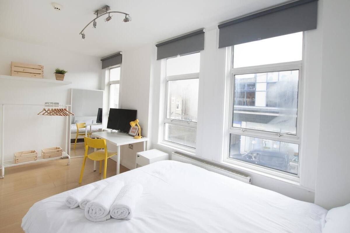 Une chambre d’hôtel équipée d’un lit, d’un bureau, d’une chaise, d’une télévision et de grandes fenêtres.