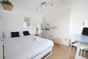 Un dormitorio con cama, escritorio, silla, armario y una planta colgante.