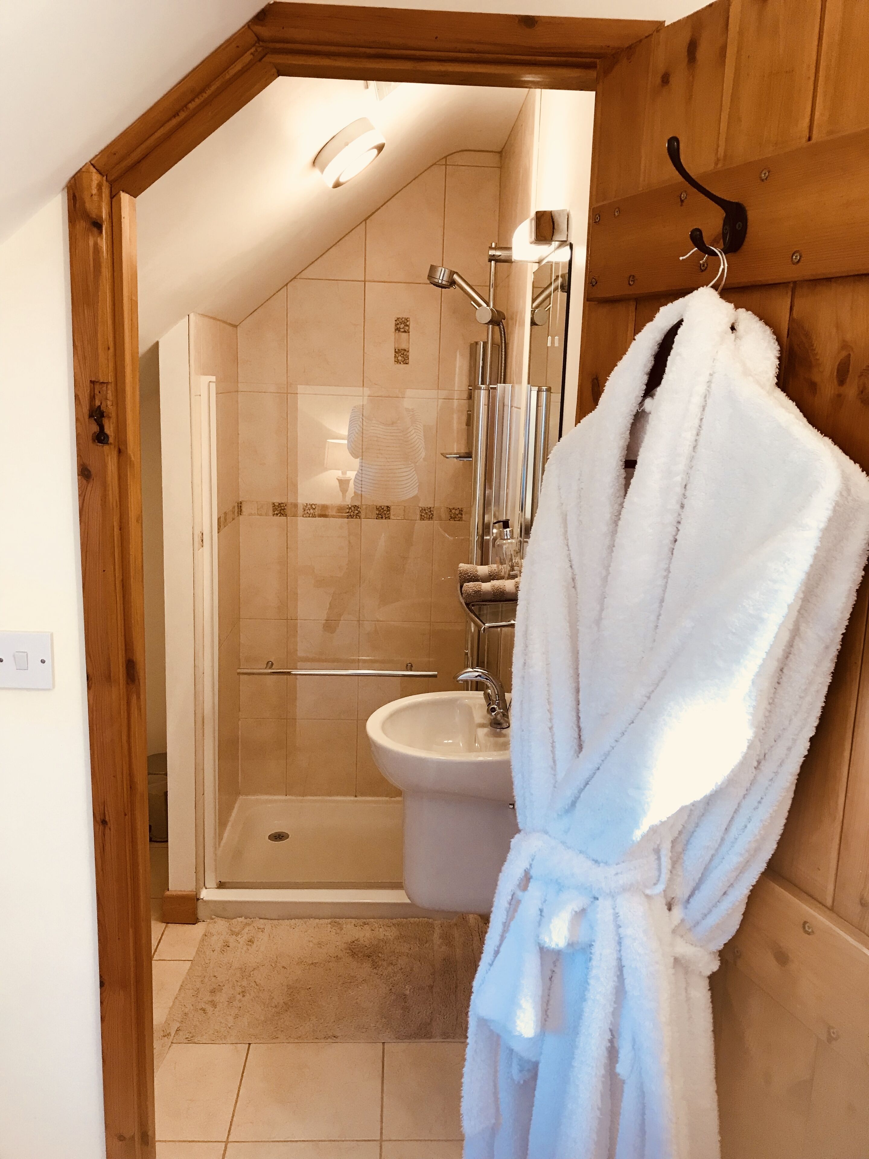 Une salle de bain avec une douche à parois de verre, un lavabo blanc et un cadre de porte en bois.