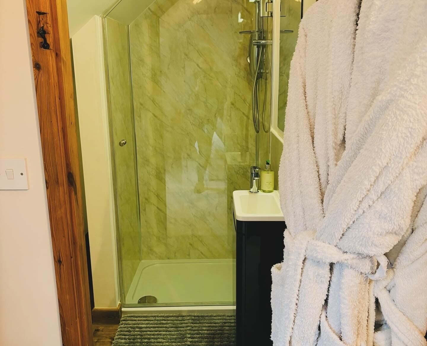 A bathroom with a glass-enclosed shower, a sink with toiletries, and a wooden door.