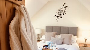 Un dormitorio con cama, mesita de noche, lámpara, bata colgada en un perchero de madera y una decoración en la pared.