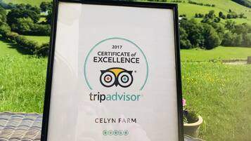 A framed TripAdvisor certificate of excellence for Celyn Farm, set against a scenic hillside backdrop.