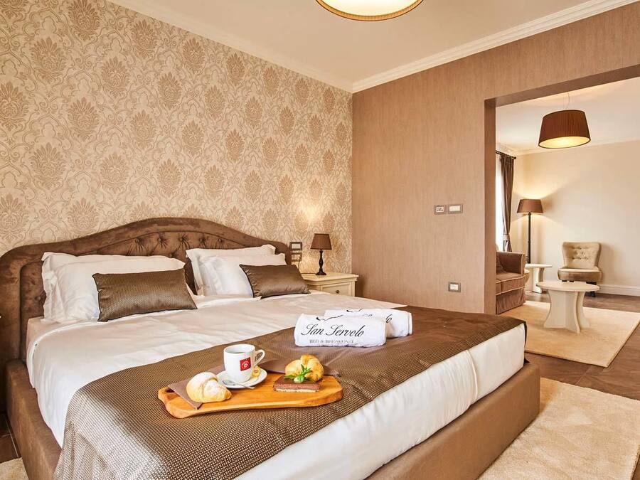 Ein Hotelzimmer mit einem großen Bett, einem Nachttisch aus Holz, einem Tablett mit Frühstücksgegenständen und Blick ins Badezimmer.
