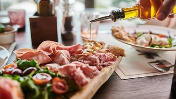 Una tabla de madera con diversos embutidos y una ensalada, mientras se vierte aceite de oliva.