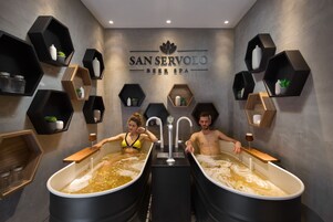 Un área de spa con dos tinas grandes, estantes con plantas y un letrero que dice "SAN SERVOLO BEER SPA".