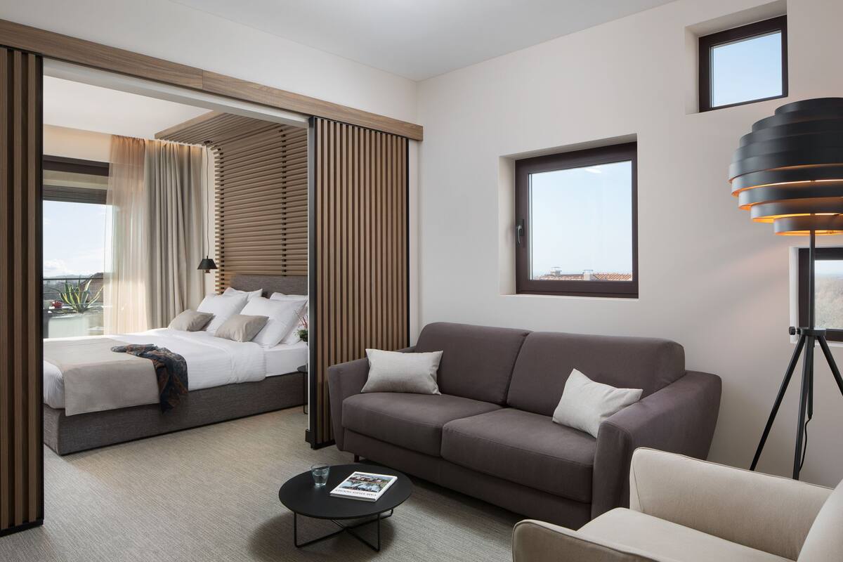 Une chambre d’hôtel moderne avec un lit, un canapé, une table basse et une grande fenêtre.