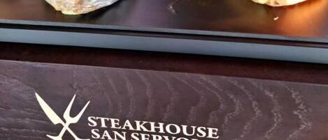 A person preparing food on a hot griddle, wearing gloves, with a logo for Steakhouse San Servolo visible.