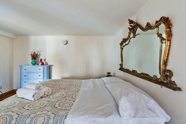 Un dormitorio con un espejo grande y ornamentado, un aparador azul, una colcha estampada y toallas dobladas con cuidado.