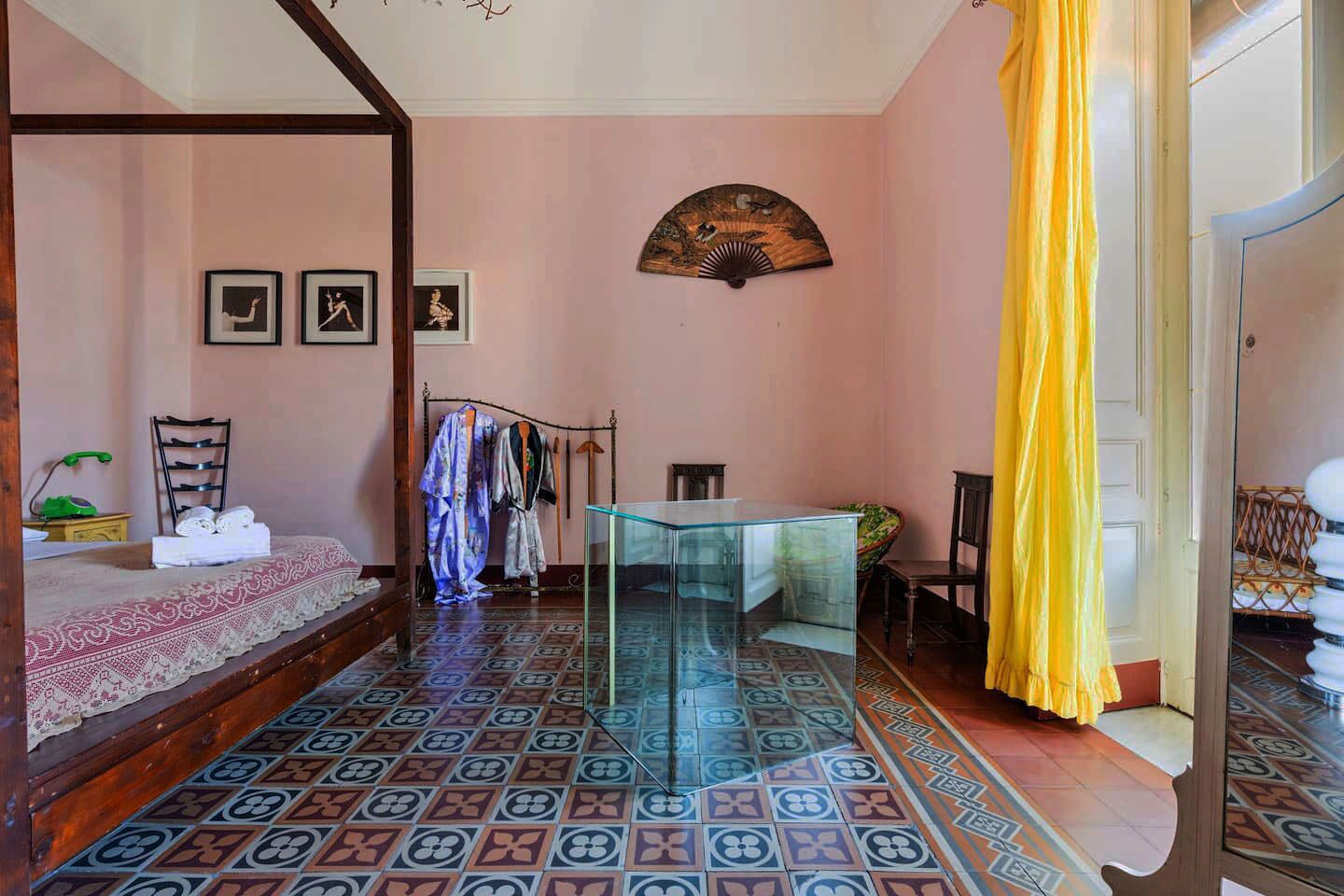 A room with a bed, a glass table, a fan, and a chair.