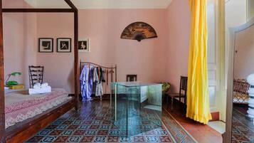 A room with a bed, a glass table, a fan, and a chair.