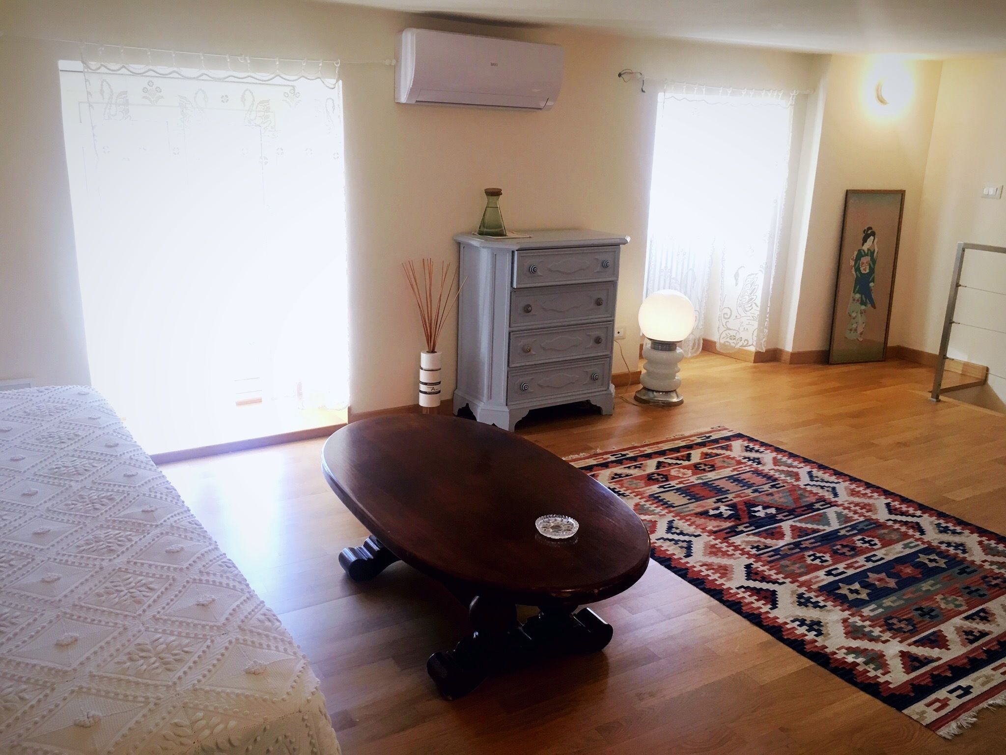 A bedroom with a bed, a wooden floor, a dresser, a lamp, and a rug.