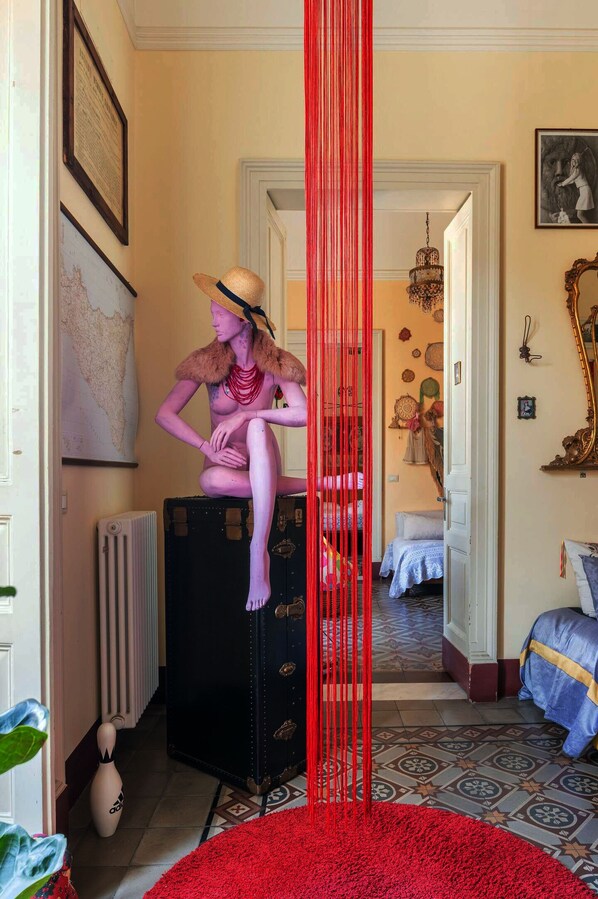 A room with a mannequin on a suitcase, a red curtain, and a map on the wall.