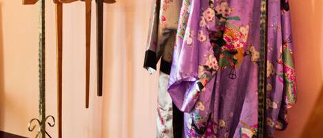 Un perchero con varias prendas de vestir, incluyendo una bata estampada con flores, en una habitación con piso de madera y pared rosa.