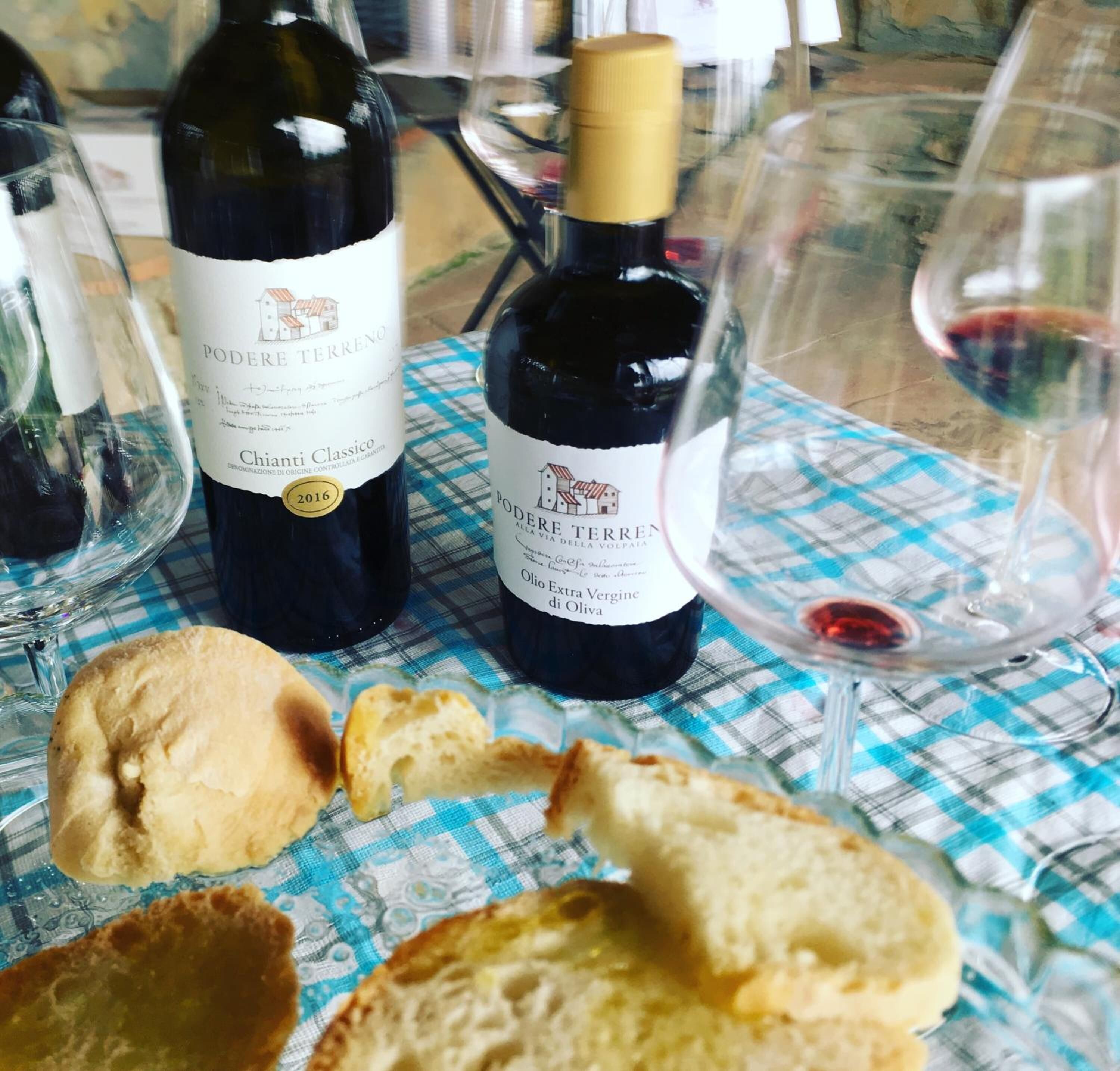 Two bottles of Chianti Classico wine and a glass of red wine on a checkered tablecloth with bread.