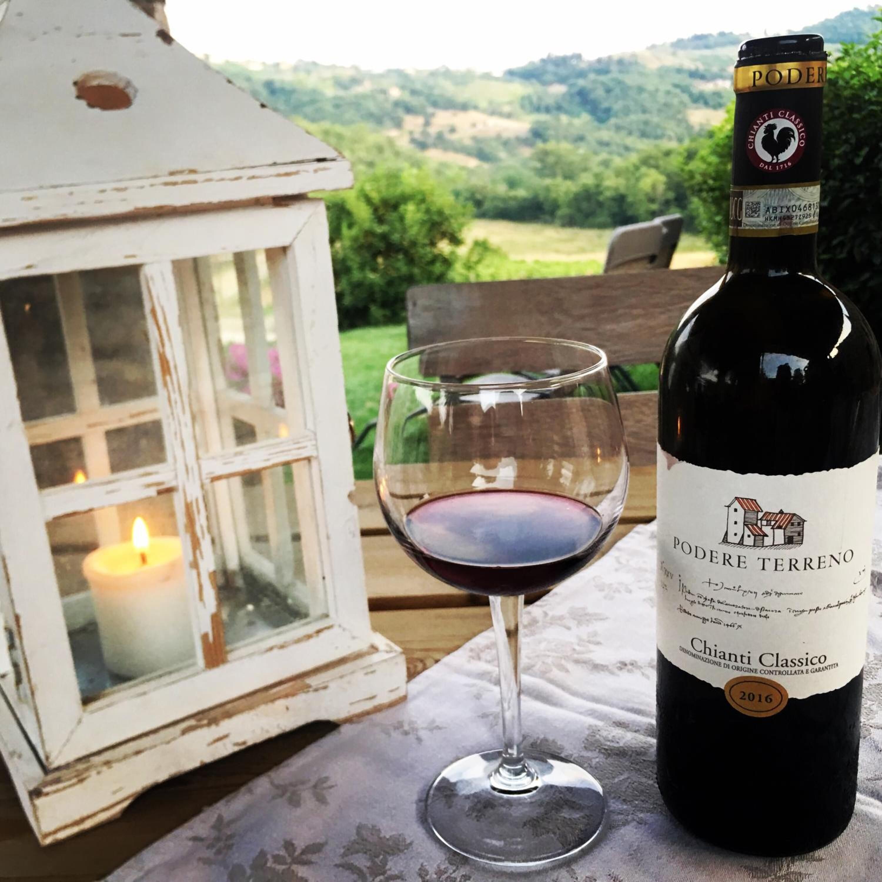 A bottle of Chianti Classico wine and a glass of red wine on a table with a white lantern and candle.