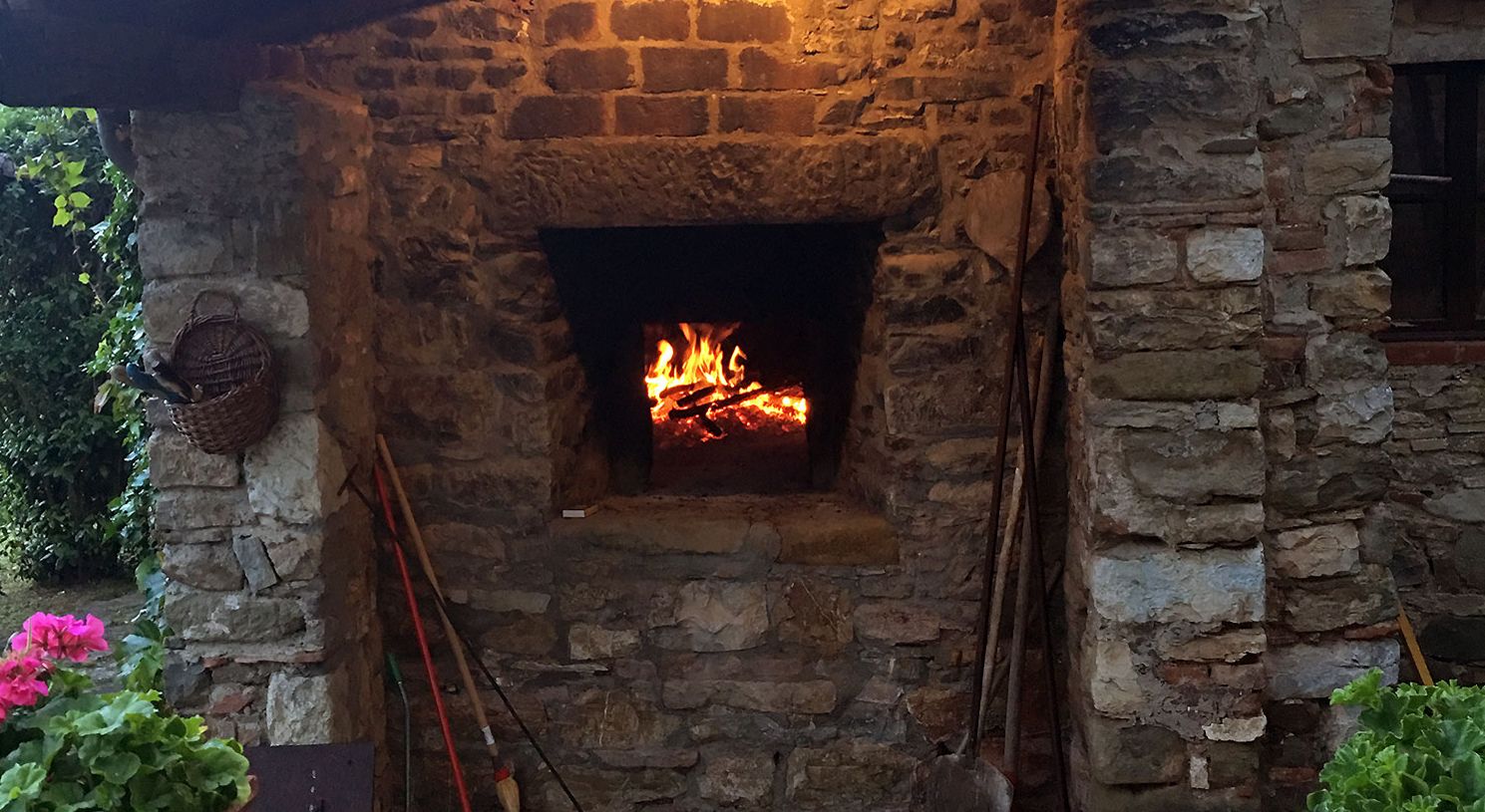 A stone fireplace with a fire burning inside, surrounded by stone walls and a basket on the left.