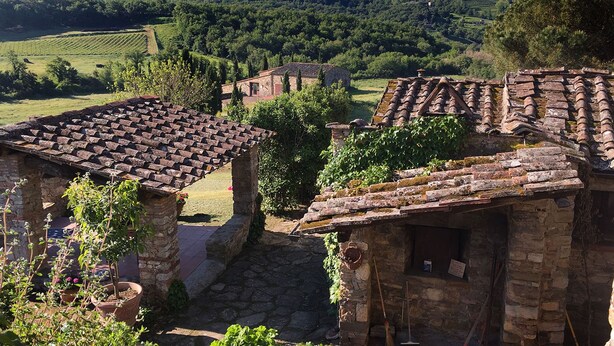 Un edificio de piedra rústico con tejado de baldosas, rodeado de vegetación y un paisaje montañoso.
