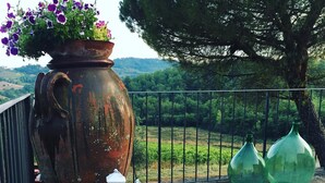 Un entorno rústico al aire libre con una maceta grande de flores, un farol blanco y dos botellas verdes sobre un patio de ladrillo.