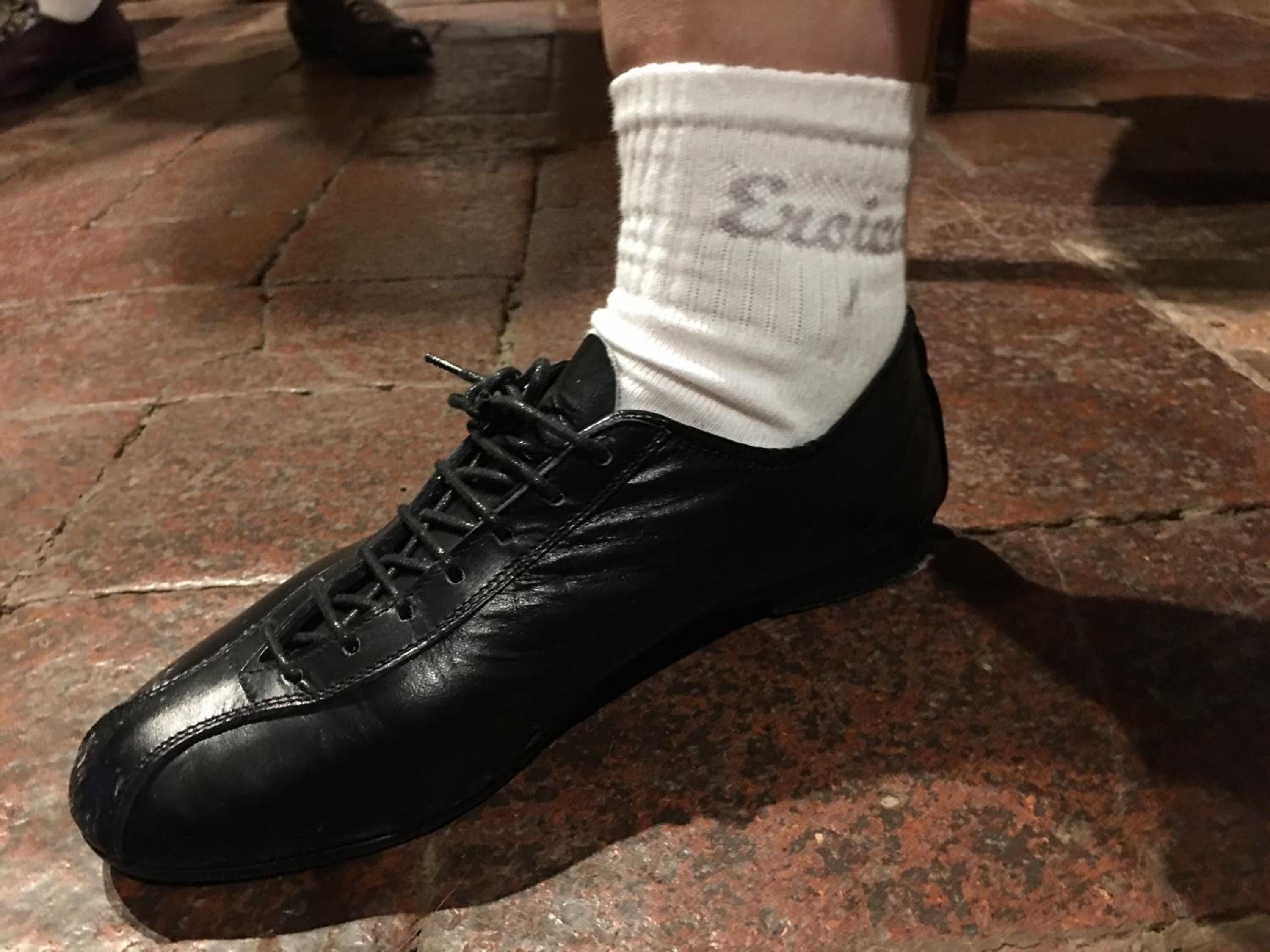 Ein schwarzes Lederschuh mit Schnürsenkeln und eine weiße Socke mit Schrift darauf.