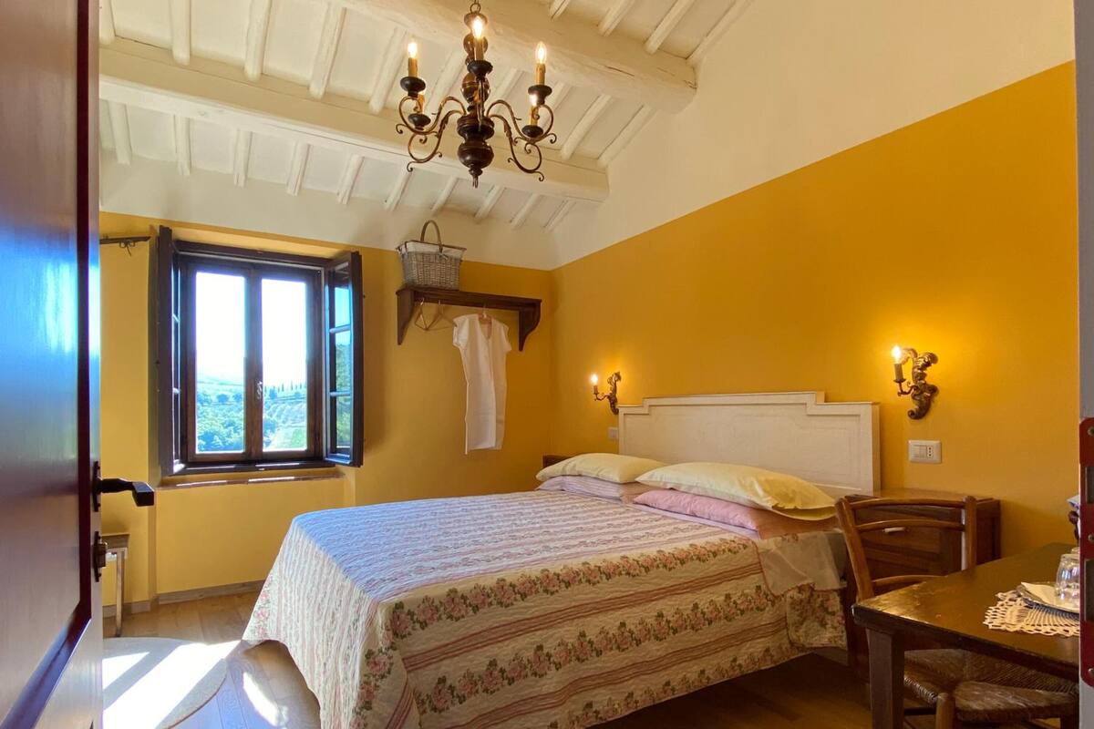 A bedroom with a bed, a window, a chandelier, a table, and a chair.