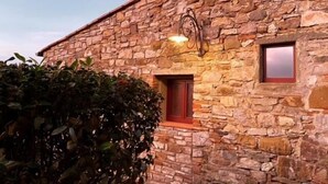 Un edificio de piedra con una ventana y una puerta, rodeado de follaje.