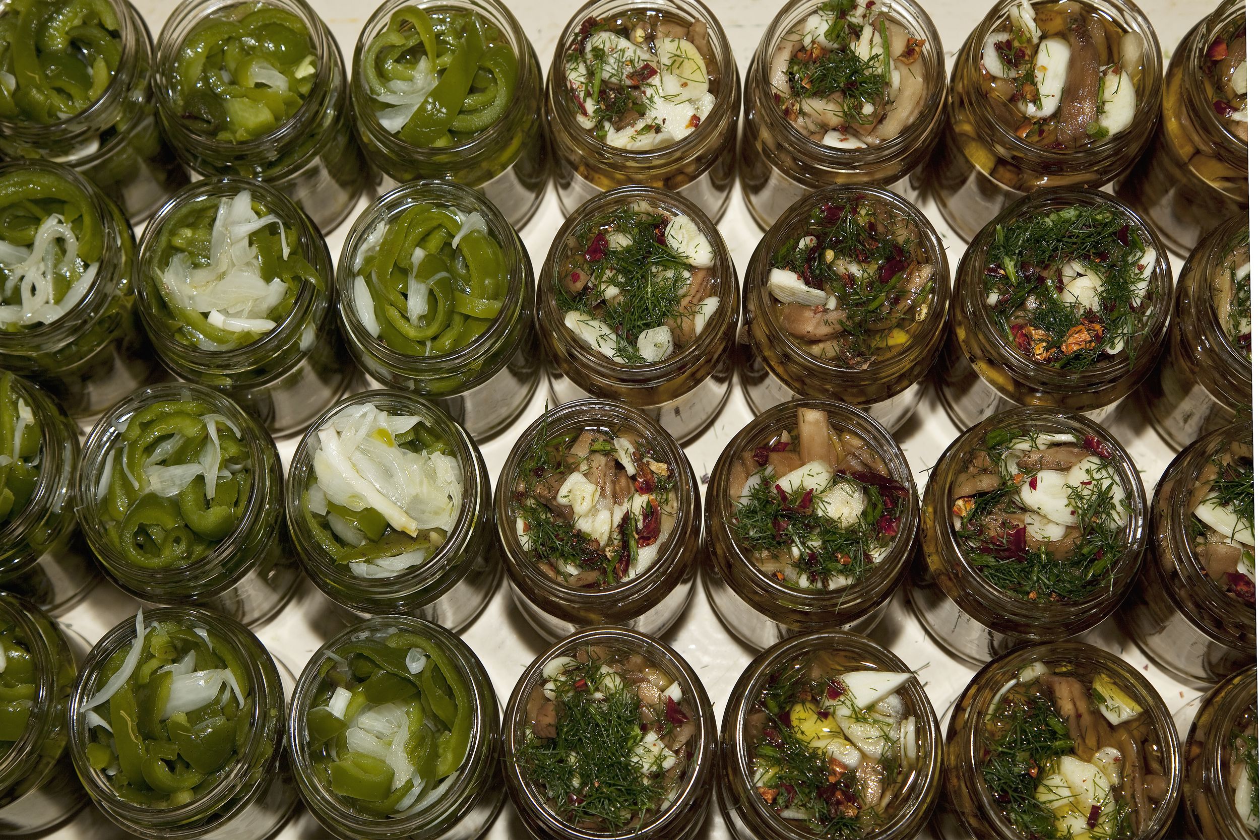 A tray of glass jars containing pickled vegetables and herbs.