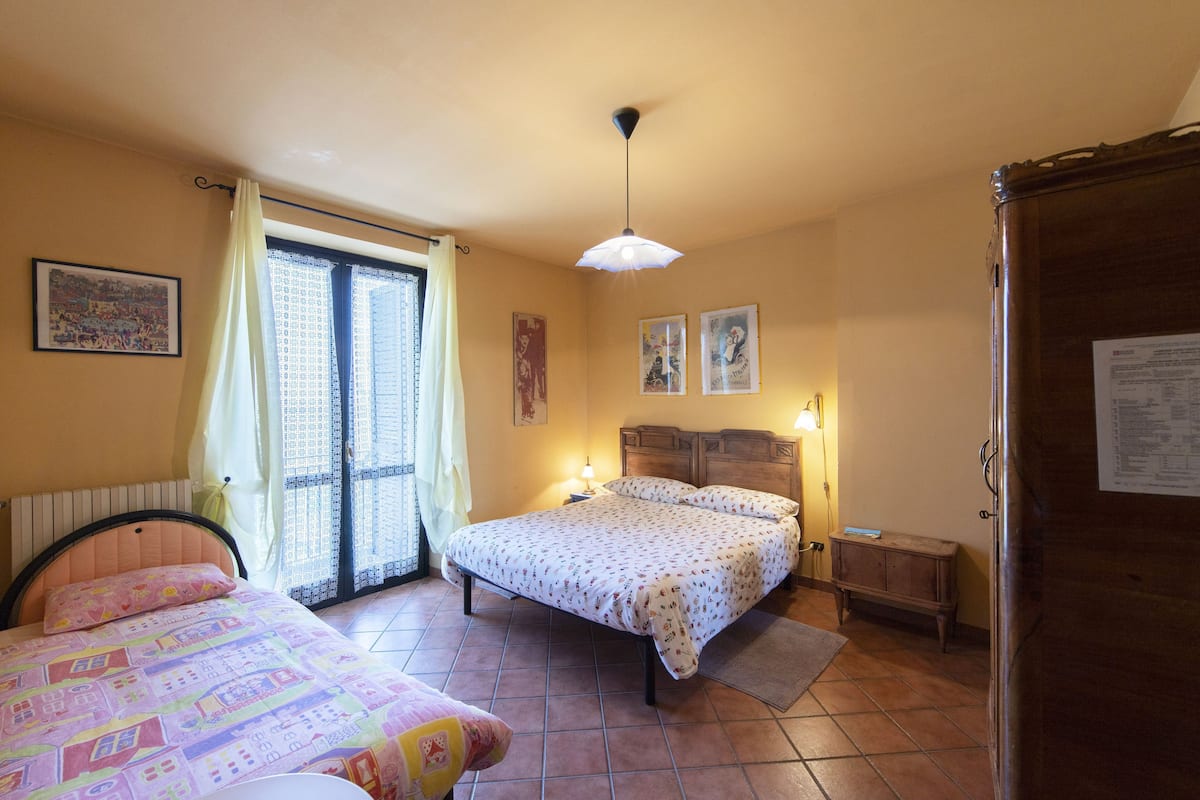 Une chambre à coucher comprenant un lit, une table de chevet, une commode, une fenêtre avec des rideaux et un luminaire au plafond.