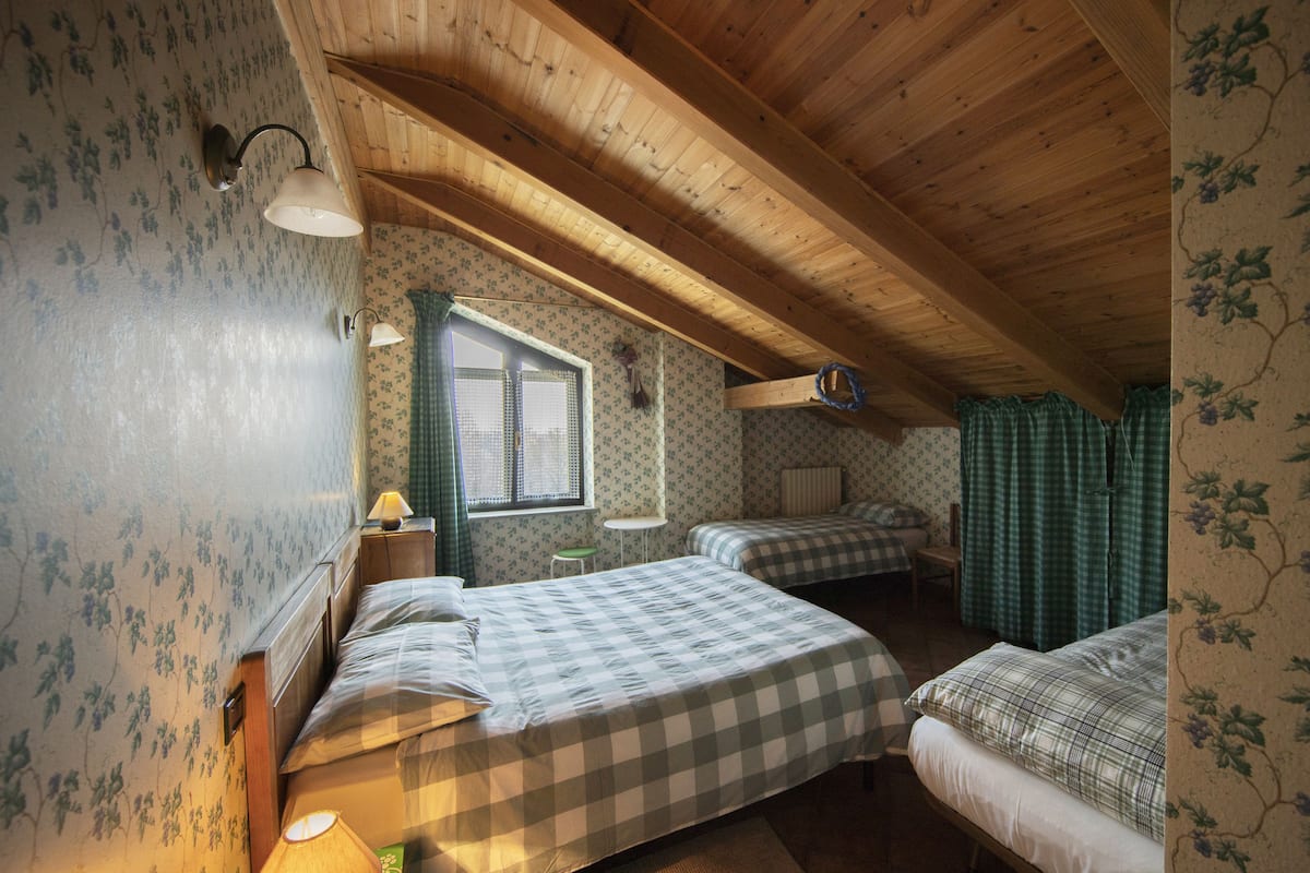 Une chambre confortable située dans les combles, avec deux lits, une fenêtre et des poutres en bois.