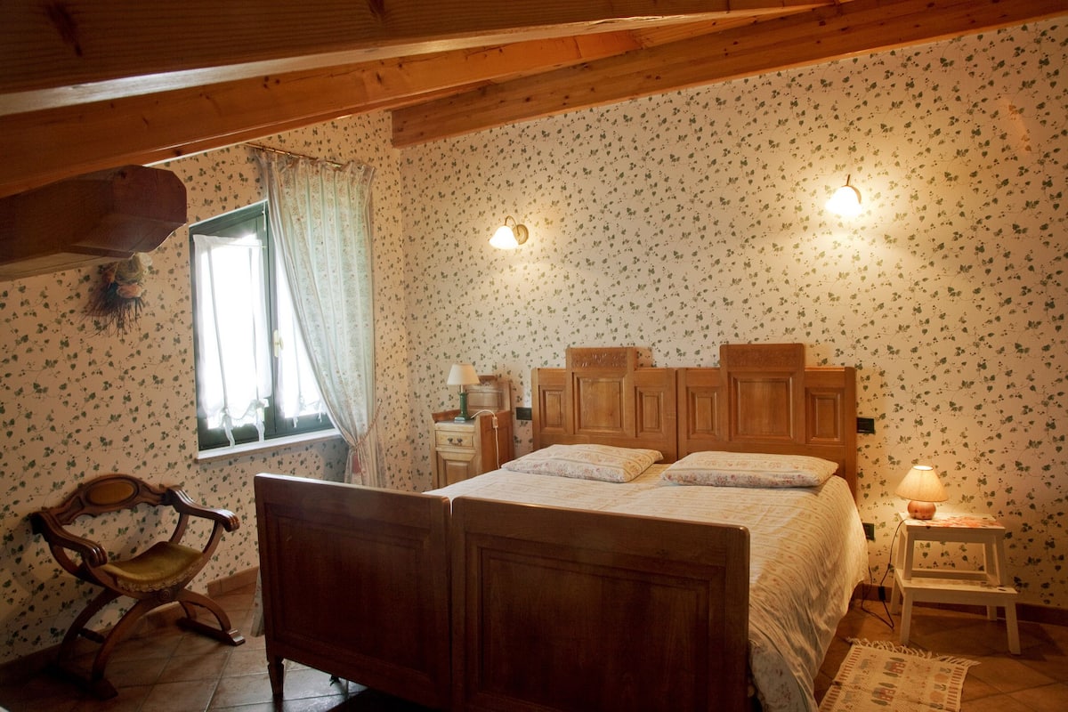 Une chambre à coucher avec un lit en bois, une chaise, une table de chevet et une fenêtre avec des rideaux.