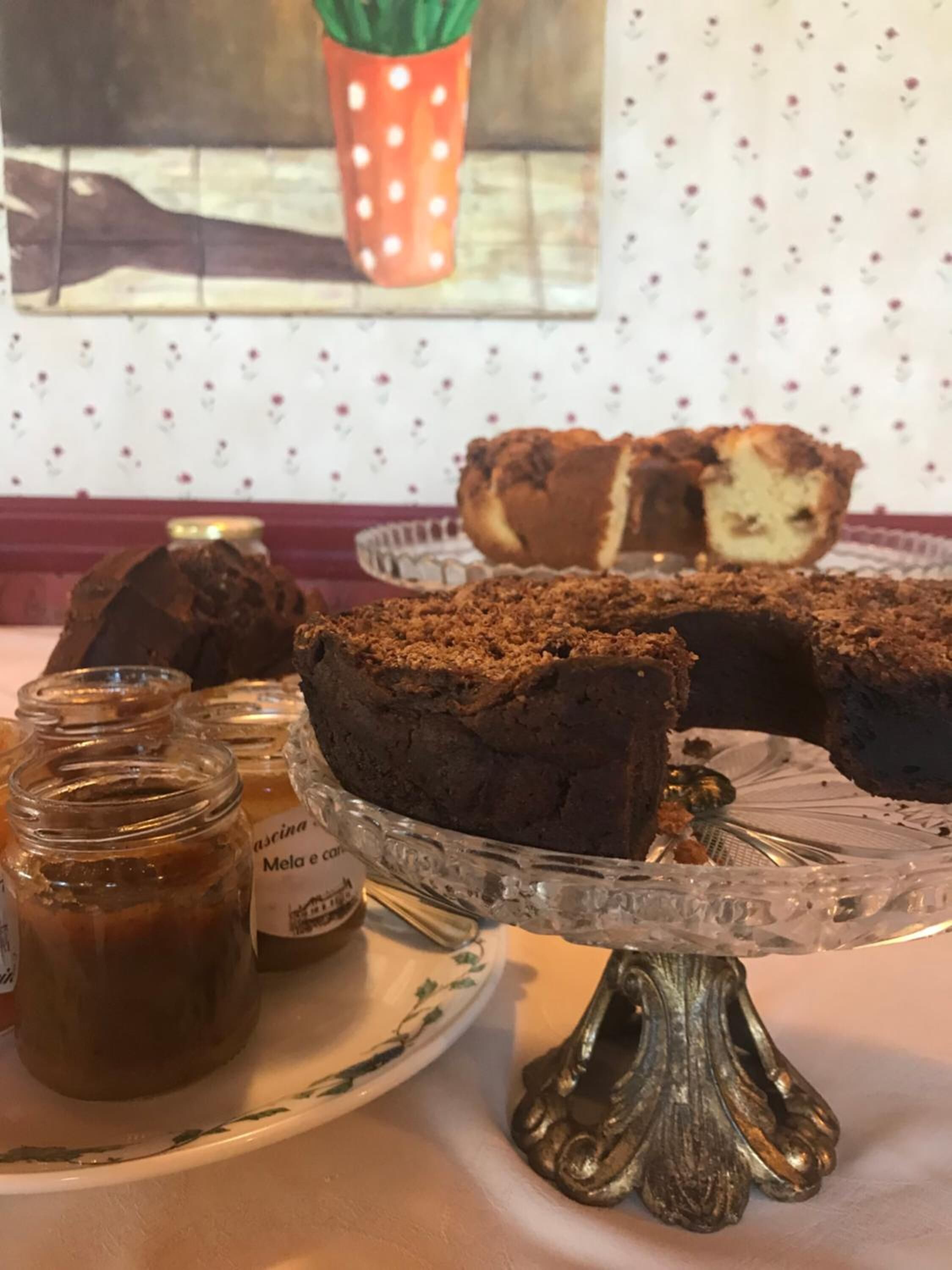 Una mesa con un soporte para pasteles, una rebanada de pastel, dos frascos de mermelada y un plato decorativo.