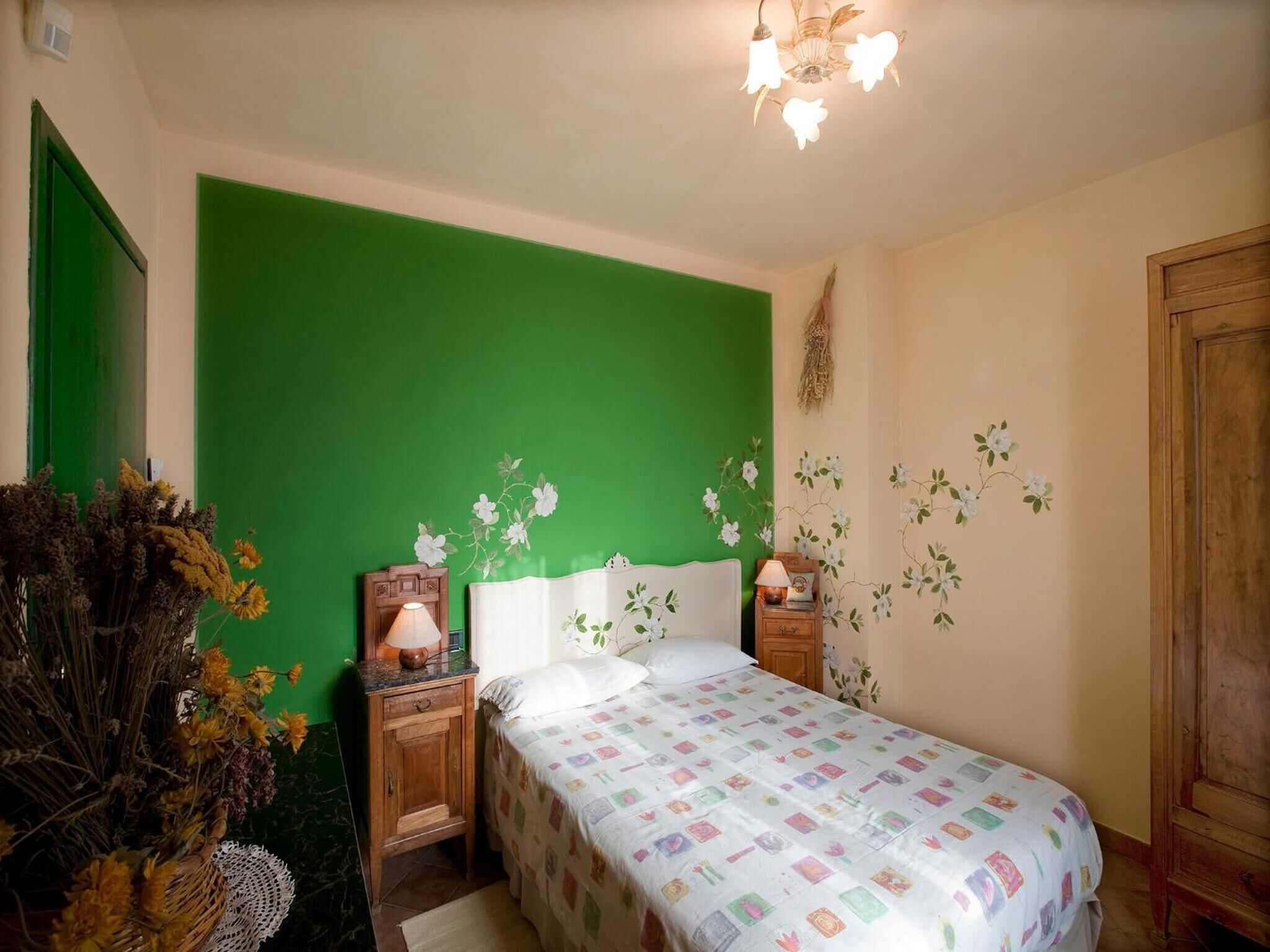 Un dormitorio con una pared verde de acento, una cama con colcha colorida, una mesita de noche con lámpara y una pieza decorativa en la pared.