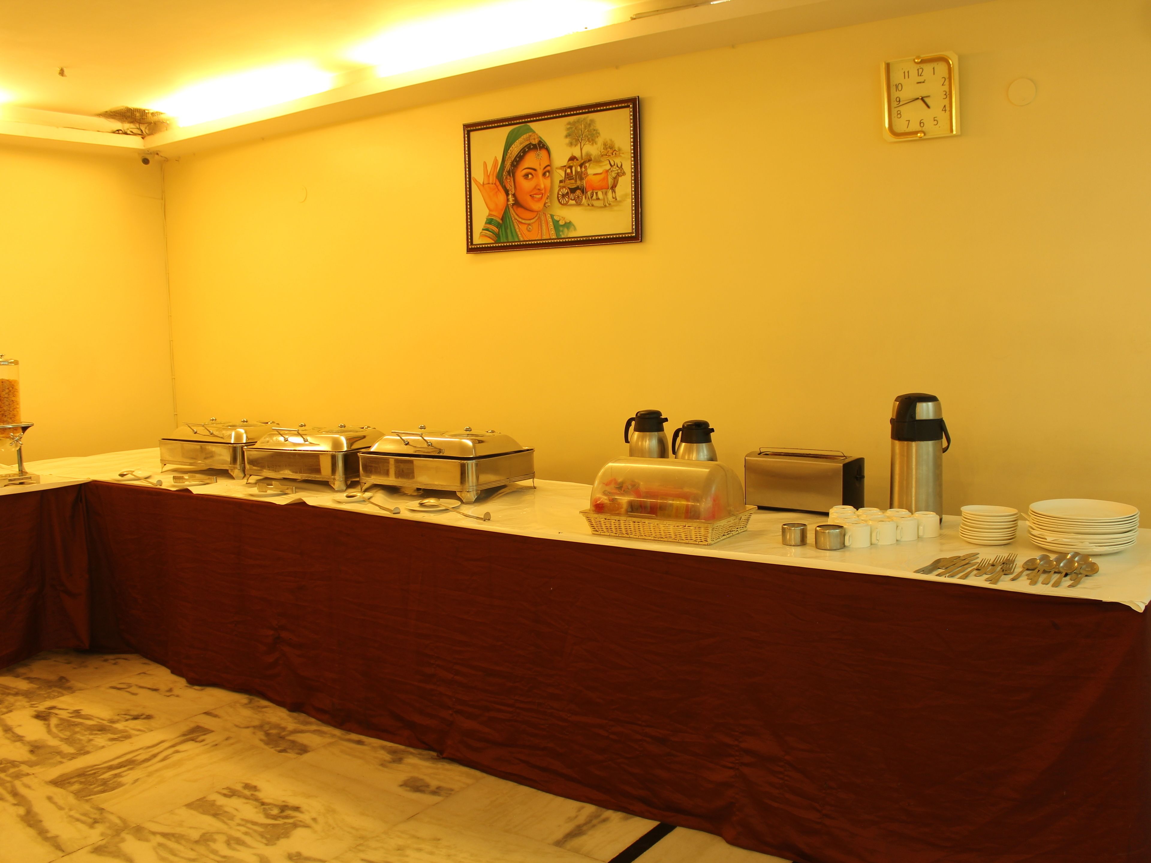 A buffet setup with food service items, a clock, and a framed picture on the wall.