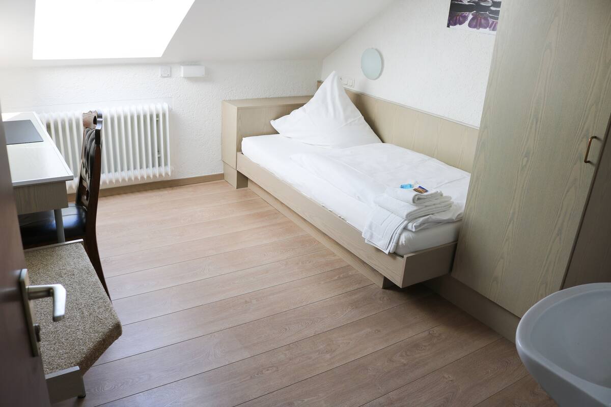 Une petite pièce bien éclairée, avec un lit simple, un bureau et un radiateur.