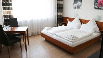 A hotel room with a wooden bed, a desk with a chair, and a window with sheer curtains.