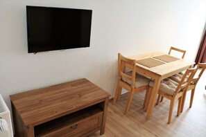 A room with a wooden dining table, four chairs, a TV mounted on the wall, and a small wooden cabinet. - Hotel Linnert (Weiterstadt)