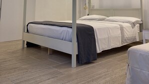 Quarto moderno com cama de dossel, paredes brancas e piso de madeira.