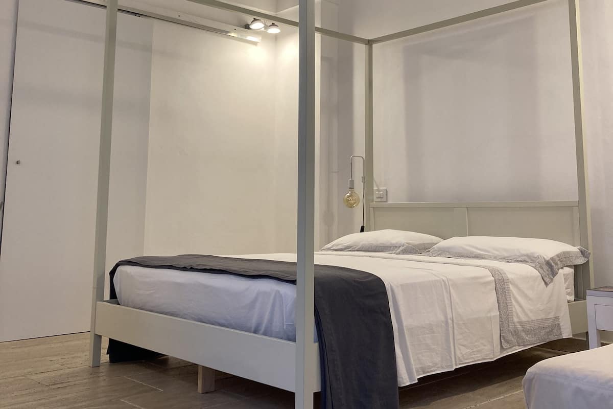A modern bedroom with a four-poster bed, white walls, and a wooden floor.