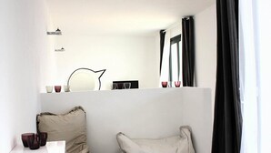 Quarto minimalista com parede branca, um pequeno aparador com objetos decorativos, uma janela com cortinas pretas e piso branco.