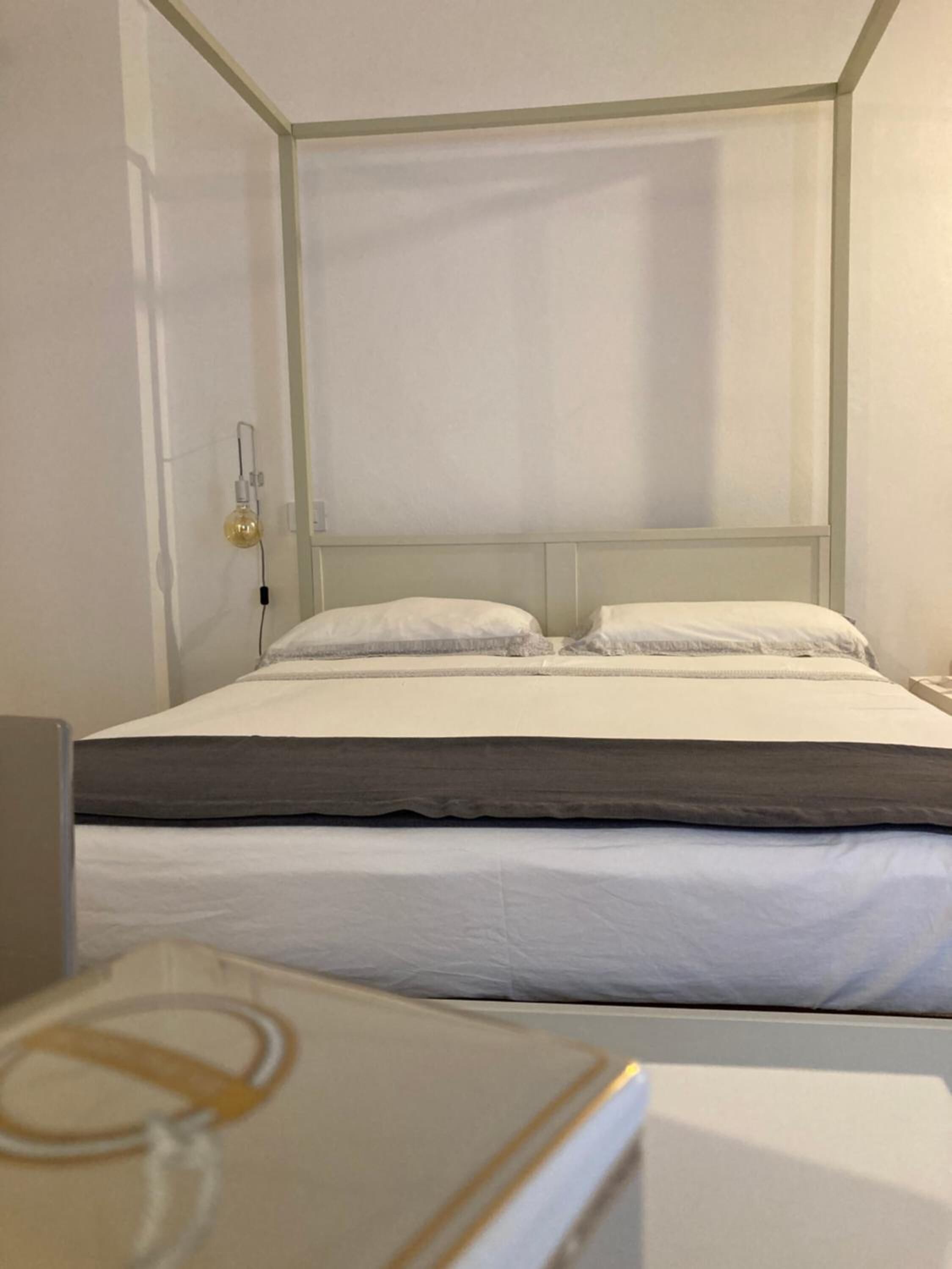 A single bed with a grey headboard and white bedding in a room with plain walls.