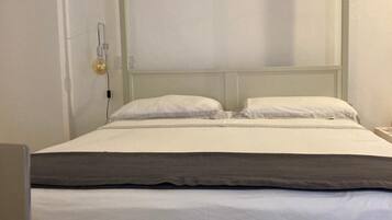A single bed with a grey headboard and white bedding in a room with plain walls.