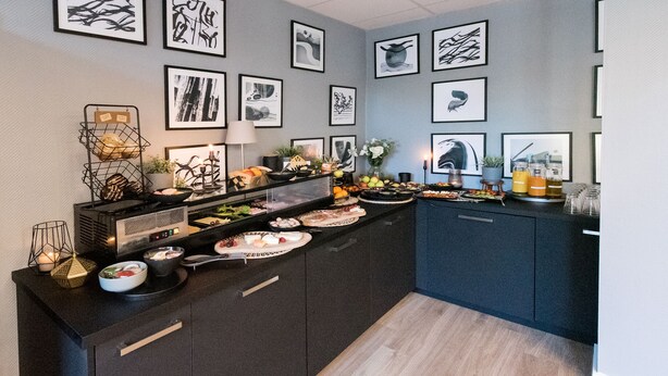 A modern kitchen with a central island, black cabinets, and a grey backsplash with framed artwork. -  DORMERO Hotel Xanten (Xanten)