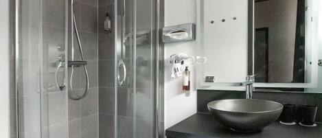 A modern bathroom with a glass-enclosed shower, a black countertop, a large sink, and a mirror.