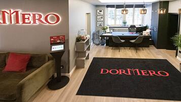 Ein moderner Arbeitsbereich mit Empfangstresen, Essbereich und einer Rezeption mit einer schwarzen Matte mit dem Schriftzug „DORMITORO“.